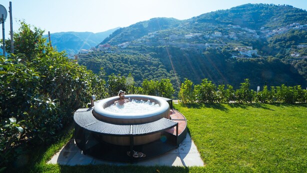 A hot tub in a lush garden with a scenic hillside view.