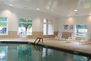 Piscina interna com água cristalina, rodeada por cadeiras de descanso brancas e um aviso sobre segurança na natação.