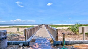 Pasarela de madera que lleva a una playa, con cielo despejado.