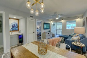 Un salon moderne avec une table à manger en bois, un canapé bleu et un téléviseur fixé au mur.