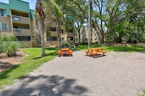 A gravel parking area with two picnic tables and a building with multiple balconies in the background.