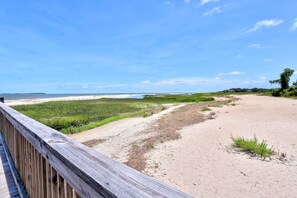 Une promenade en bois mène à une plage de sable, d’où l’on a une vue dégagée sur l’océan et le lointain rivage.