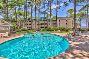 A swimming pool surrounded by lounge chairs and a building with multiple balconies.