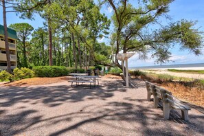 Ein Park mit Picknicktischen und Bänken, umgeben von Bäumen und Blick auf den Strand.
