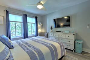 Une chambre à coucher avec un lit, une commode, une chaise, un téléviseur et une fenêtre avec des rideaux.