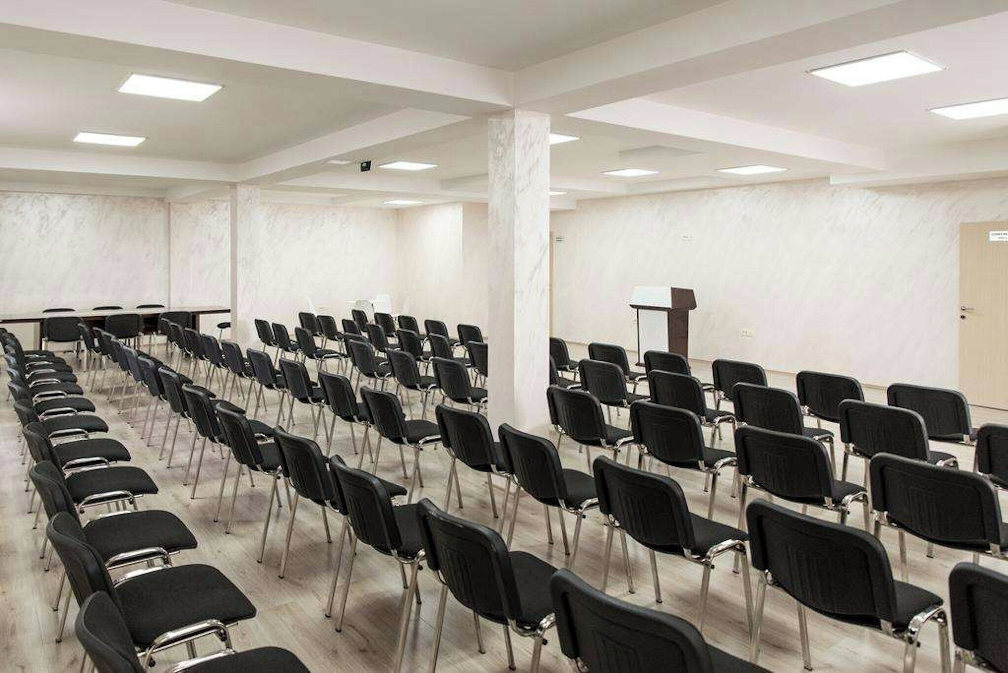 A conference room with rows of black chairs, a podium, and a whiteboard.