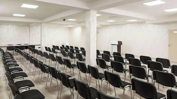 A conference room with rows of black chairs, a podium, and a whiteboard.