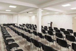 Un salón de conferencias con filas de sillas negras, un atril y una pizarra.