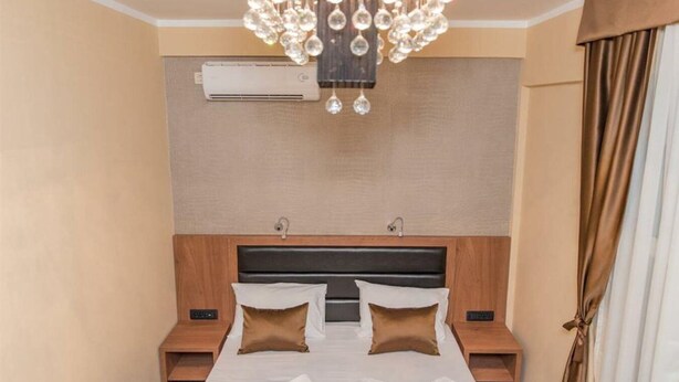 Een hotelkamer met een groot bed, twee nachtkastjes, een moderne kroonluchter, een airconditioningsysteem en een gordijn voor het raam.