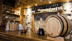 Een bar met houten planken vol flessen, een groot houten vat en twee glazen flessen op het aanrecht.