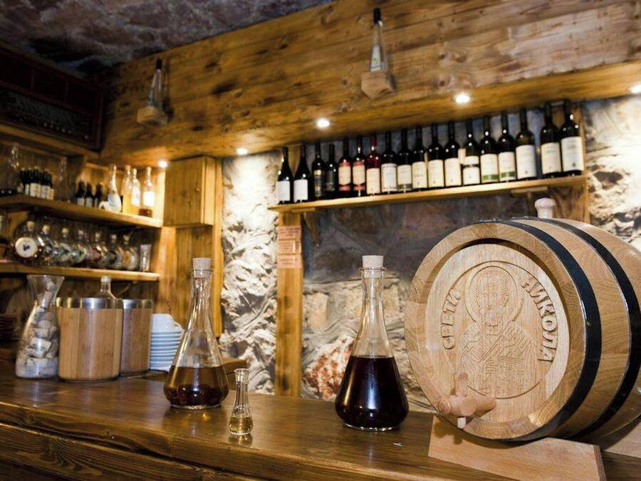 A bar area with wooden shelves stocked with bottles, a large wooden barrel, and two glass bottles on the counter.