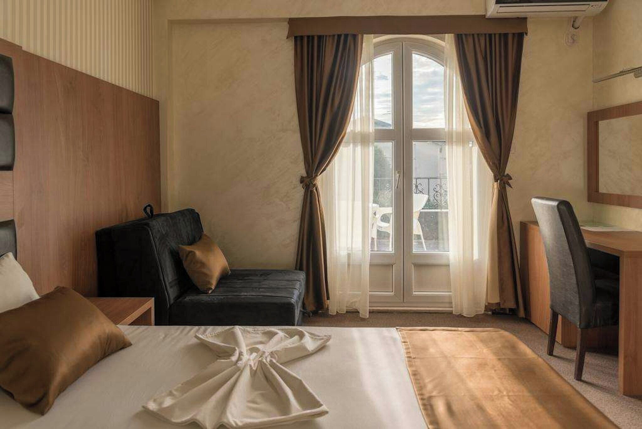 Habitación de hotel con cama, escritorio, silla y vistas al exterior a través de una ventana.