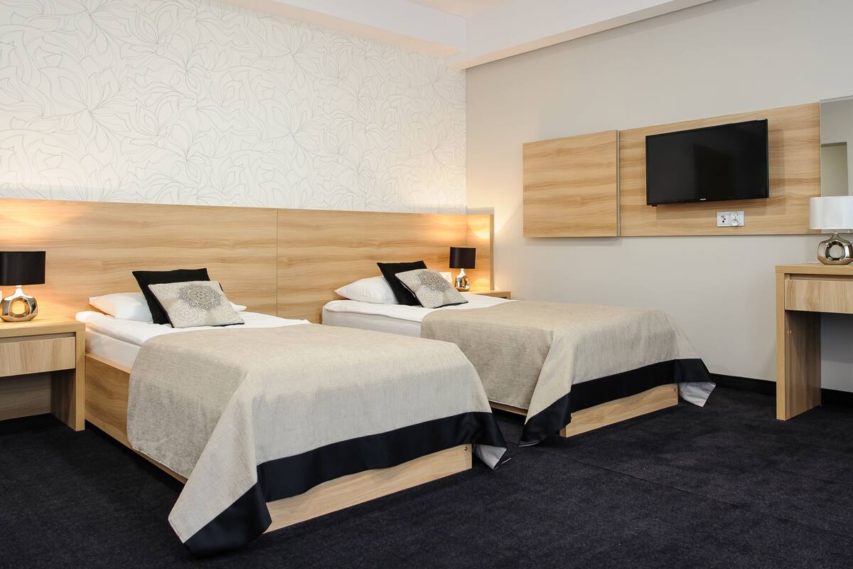 Una habitación de hotel con dos camas, un escritorio, un televisor y un espejo.