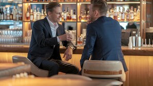 Two men in suits seated at a bar with a well-stocked liquor shelf behind them. - TeoDorka Med & Spa (Ciechocinek)