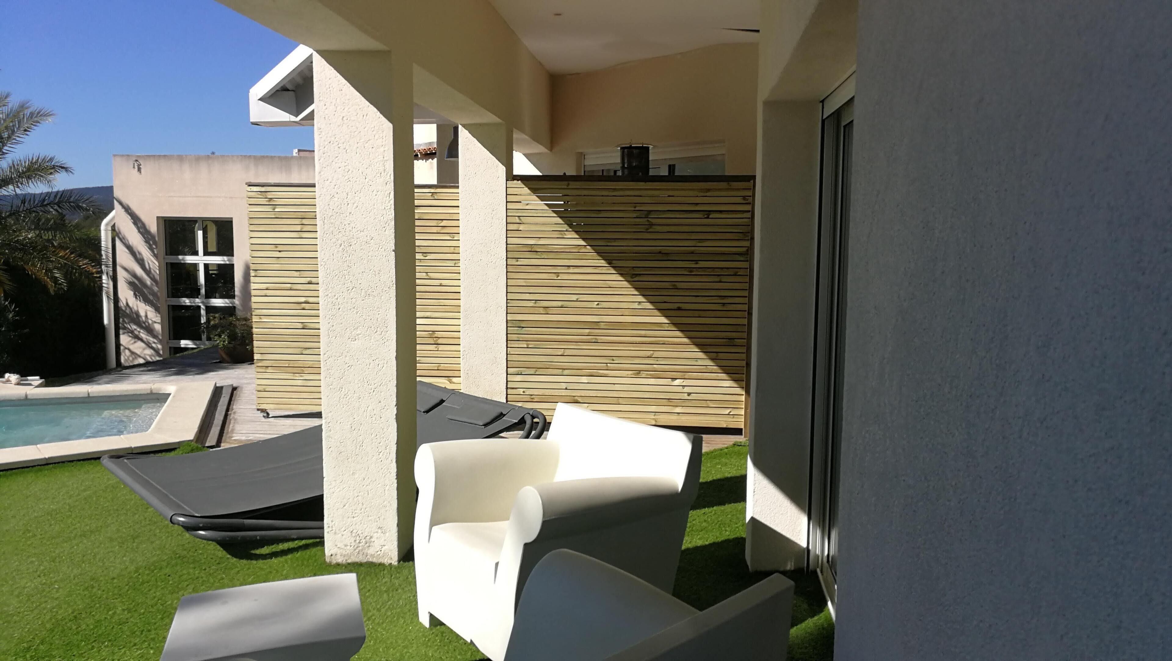 A modern outdoor patio with a pool, lounge chairs, and a wooden fence.