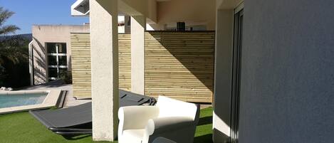 A modern outdoor patio with a pool, lounge chairs, and a wooden fence.