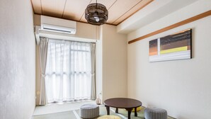 Una habitación con suelo de tatami, puertas correderas, una mesita, dos cojines y una obra de arte colgada en la pared.