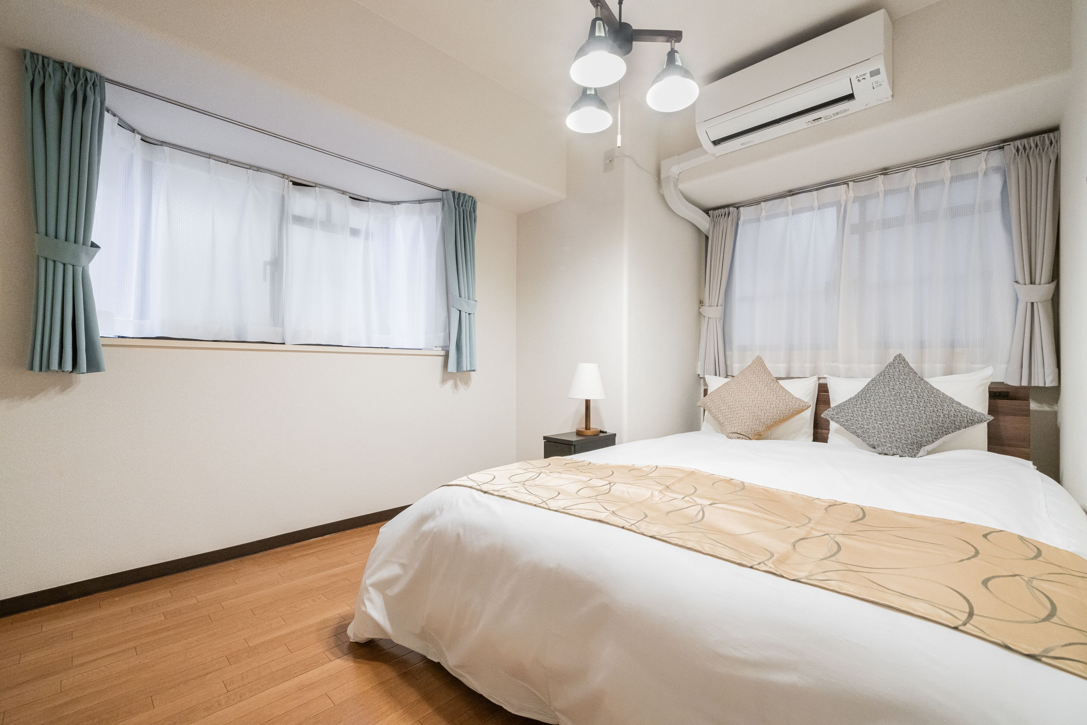 A hotel room with a large bed, two bedside tables, an air conditioner, and curtains on the windows.