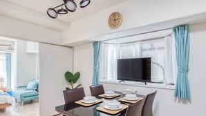 Una habitación de hotel moderna con zona de comedor, televisión de pantalla plana y un espejo grande que refleja el ambiente.