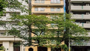 Un edificio residencial de varios pisos con balcones, un patio arbolado y un cielo despejado.