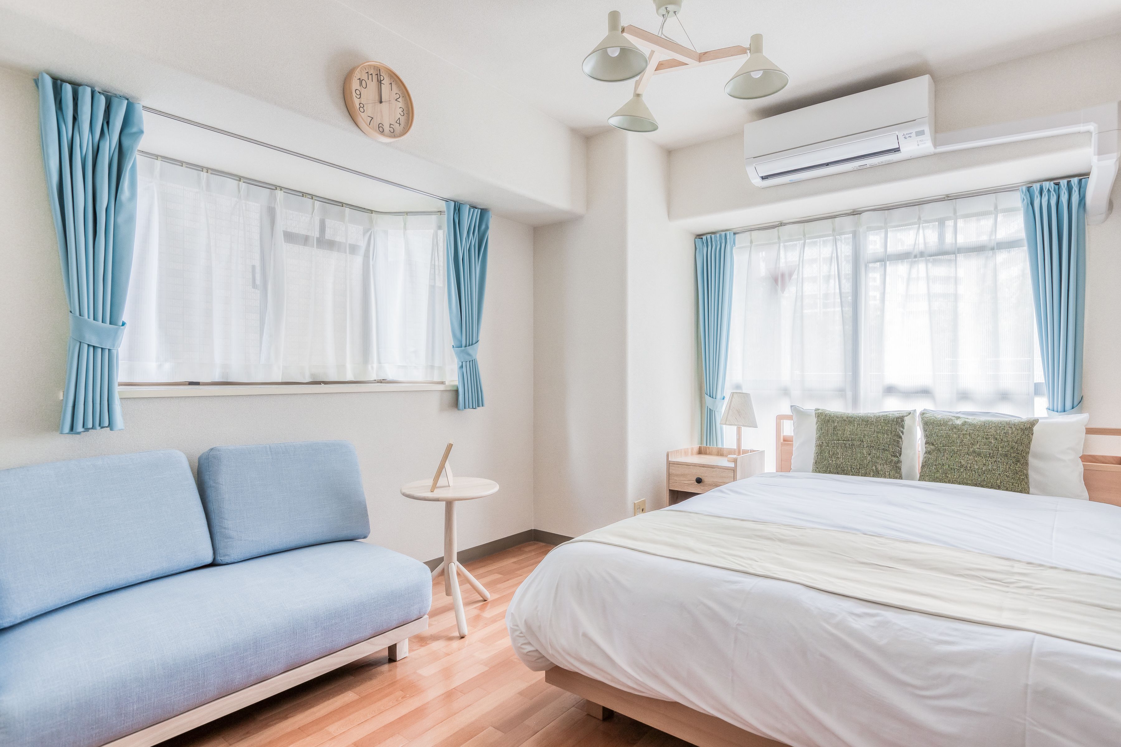 A modern bedroom with a bed, a blue sofa, a small round table, and a clock on the wall.