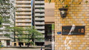 Un edificio de varios pisos con fachada de ladrillo, un letrero con caracteres japoneses y una vista de la calle con árboles y una persona caminando.