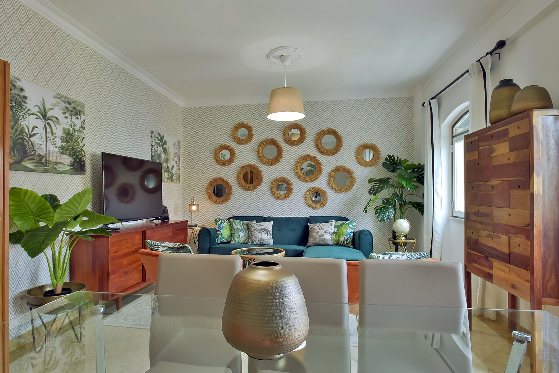 Un moderno salón con sofá, mesa de centro, televisor y espejos decorativos en la pared.