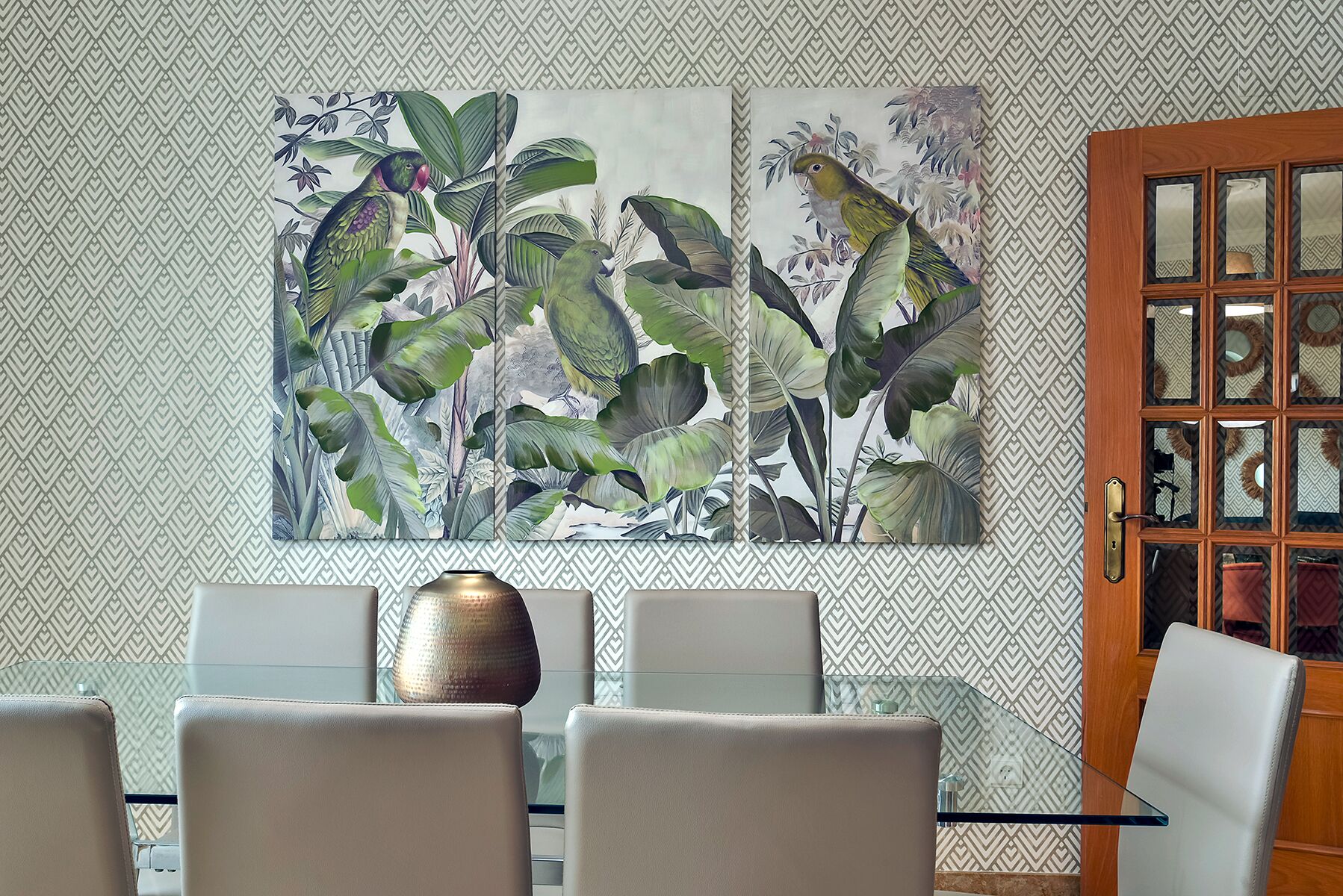 A dining area with a glass table, white chairs, and a large tropical-themed painting on the wall.