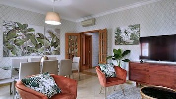 Uma sala de estar moderna com televisão, assentos e plantas decorativas.
