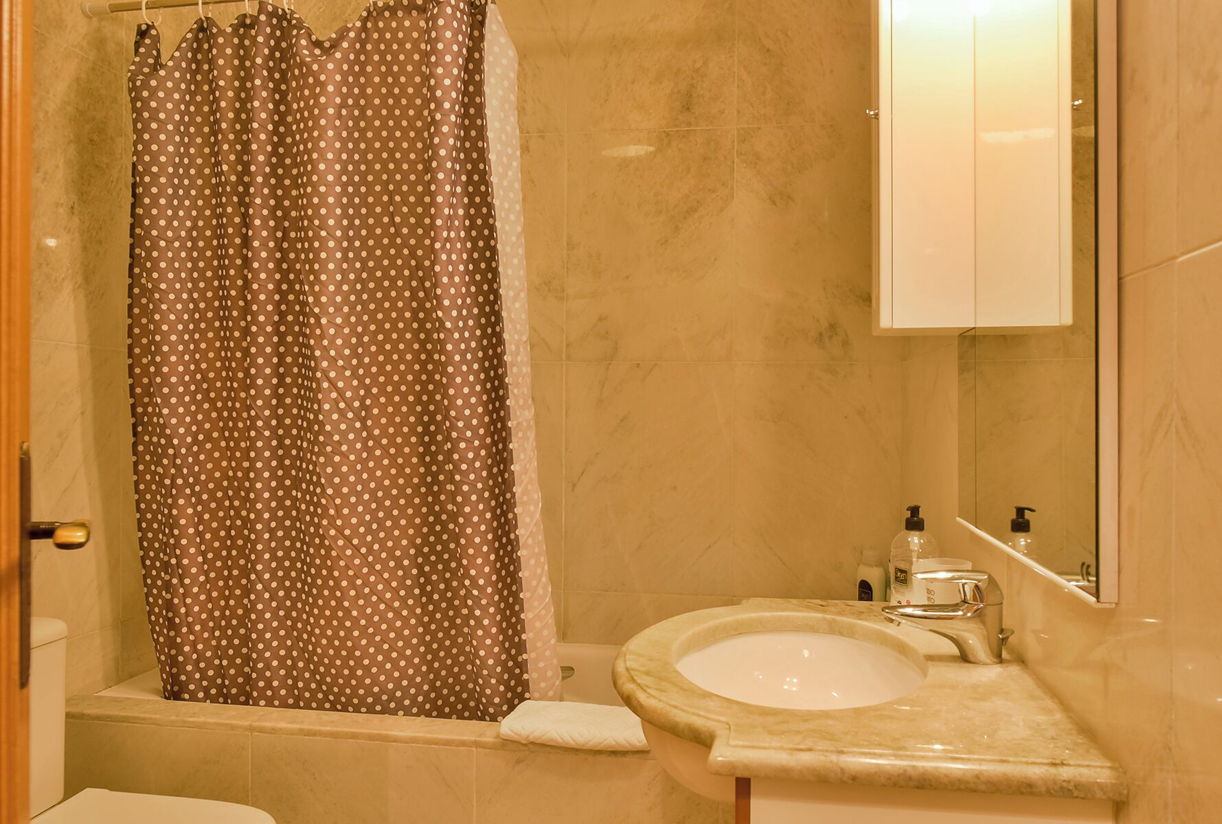 A bathroom with a shower curtain, a sink, and a mirror.