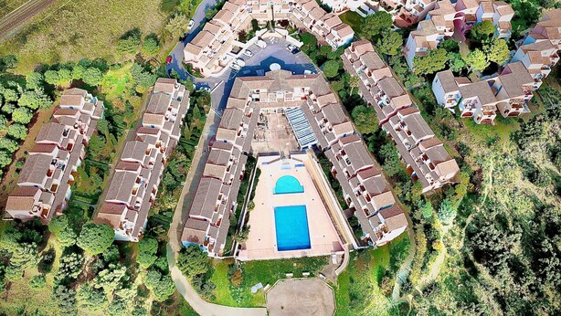 Vista aérea de un complejo residencial con varias edificaciones, una piscina central y zonas verdes circundantes.