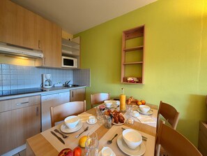 A kitchen with wooden cabinets, a microwave, and a breakfast setup including croissants, fruit, and coffee. - Appartement cosy à 500m de la Plage (Cerbère)