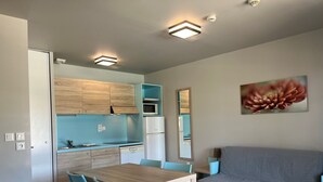 A compact living space with a kitchenette, a dining area with a wooden table and blue chairs, and a gray sofa.