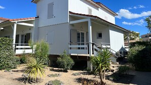 A two-story building with a balcony, a covered porch, and a small garden area with various plants.