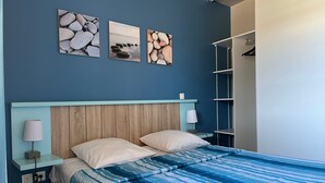 A bedroom with a bed, a nightstand, a lamp, a wardrobe, and three framed pictures on the wall.