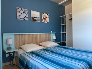 Een slaapkamer met een bed, een nachtkastje, een lamp, een kledingkast en drie ingekaderde foto's aan de muur.