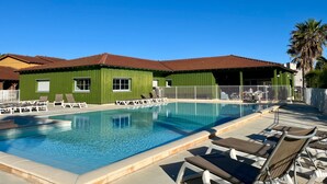 A swimming pool with lounge chairs, a green building with windows, and a clear blue sky.