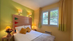 Ein Schlafzimmer mit einem hölzernen Kopfteil, zwei Nachttischlampen, einem Fenster mit Vorhängen und einem Bett mit weißen Bettwäsche und zwei Kissen.