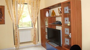 A room with a TV on a wooden cabinet, a radiator, and a window with curtains. - Casa Pierosa: pretty, private and welcoming (Frosinone)