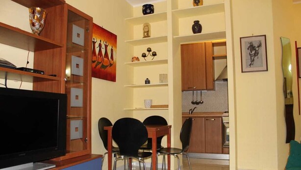 A living room with a TV, wooden shelves, a painting, and a dining area with chairs. - Casa Pierosa: pretty, private and welcoming (Frosinone)