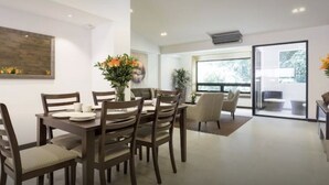 A modern dining area with a wooden table and chairs, a vase with flowers, and a view of the outdoors through large windows.