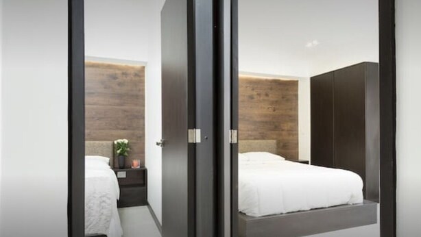 A modern bedroom with a wooden accent wall, a bed with white bedding, and a dark wardrobe.
