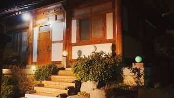 A traditional wooden building with a wooden door, windows with lattice designs, and a staircase leading to the entrance.
