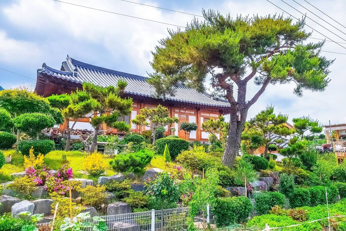 Un bâtiment traditionnel japonais, doté d’un toit recouvert de tuiles, entouré de jardins bien entretenus et de divers arbres.