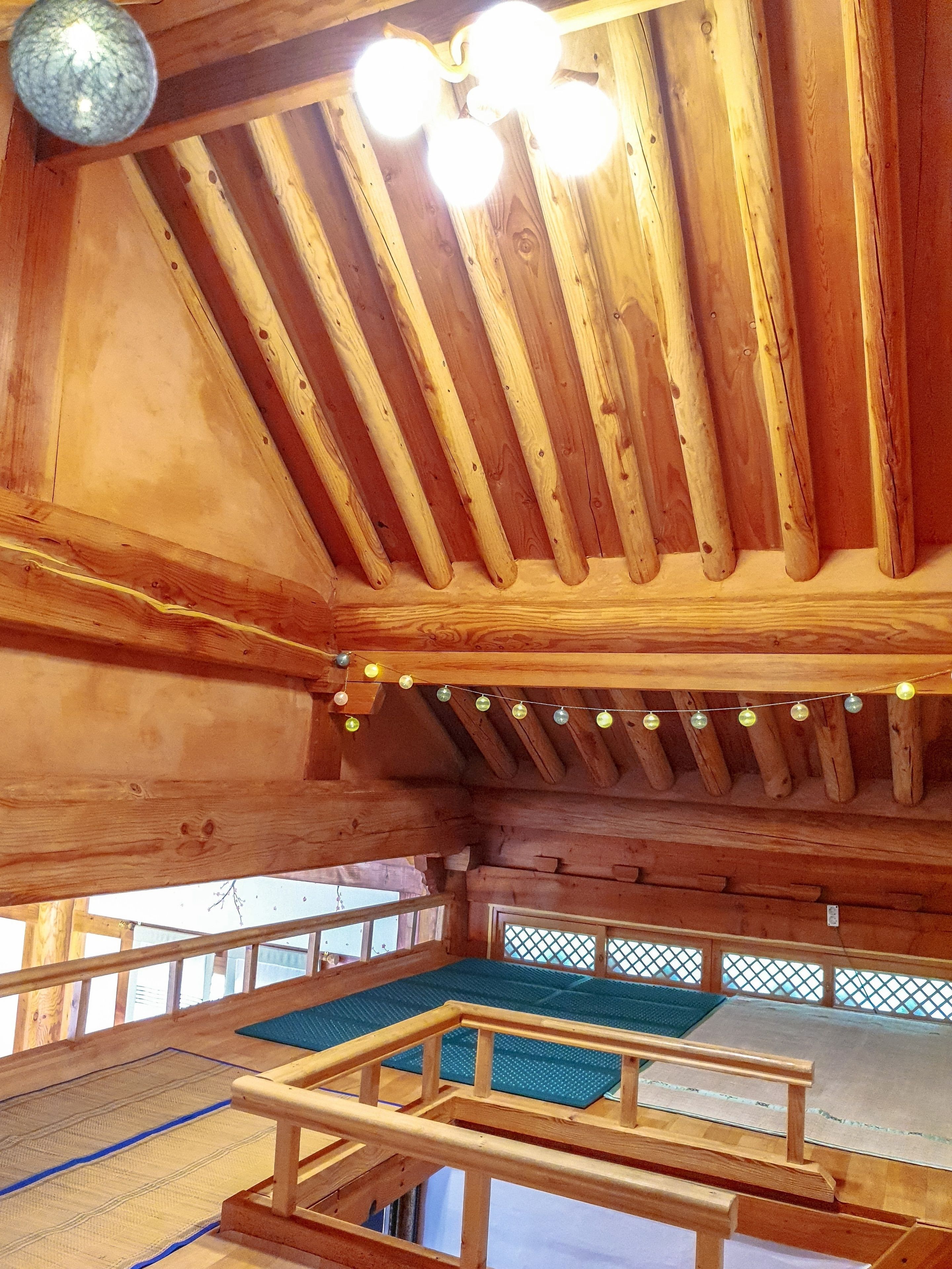 A wooden interior with a sloped ceiling, string lights, and a view through a window.