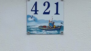 Un panneau indiquant le numéro de la maison, orné d’une illustration de bateau.