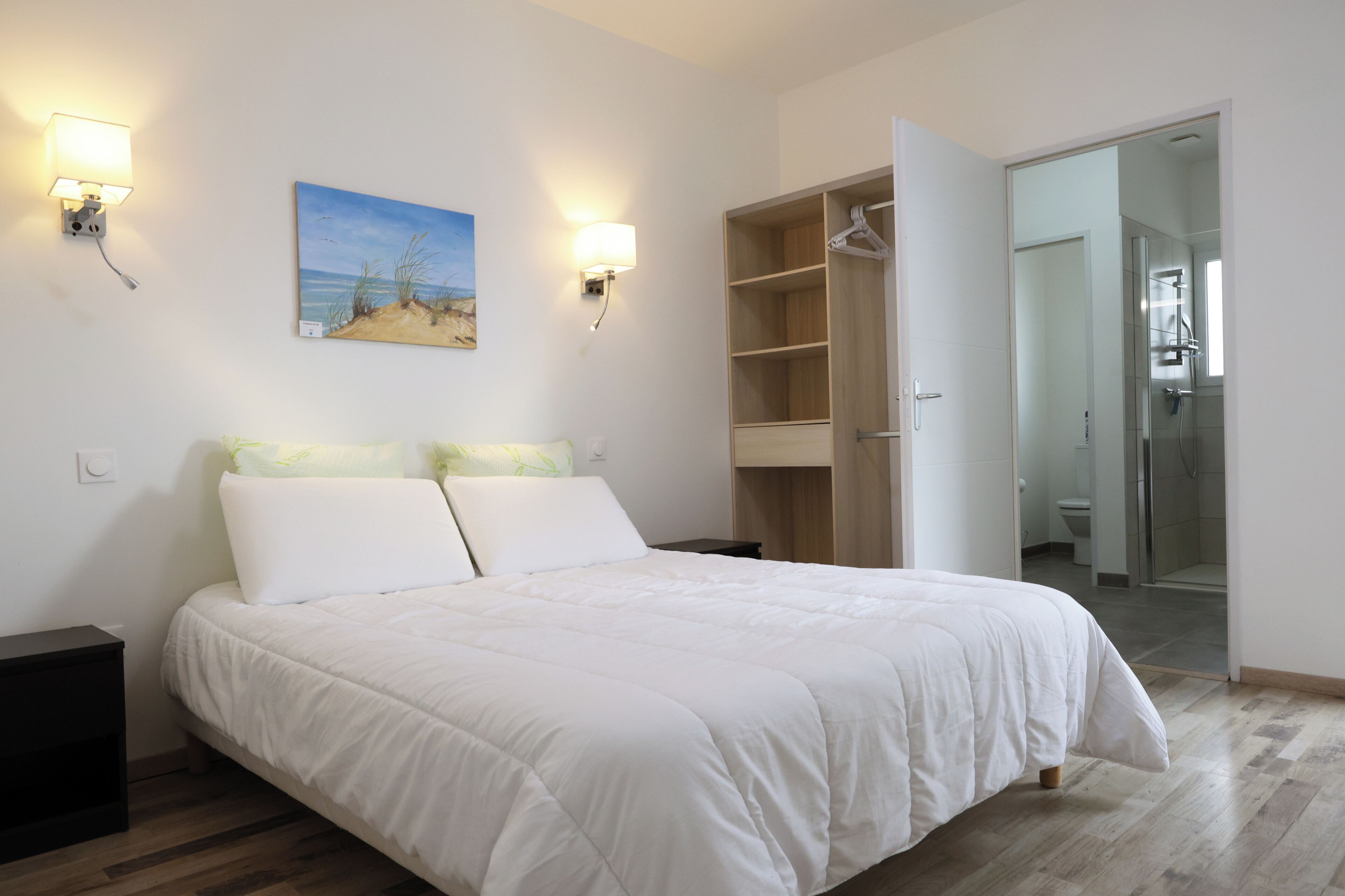Une chambre à coucher comprenant un lit, deux lampes fixées au mur, un tableau et un dressing.