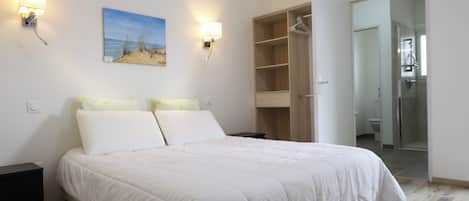 Une chambre à coucher comprenant un lit, deux lampes fixées au mur, un tableau et un dressing.