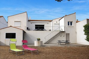 A modern building with a flat roof, a staircase leading to a balcony, and outdoor seating.