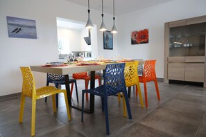 Un espace repas avec une longue table, des chaises colorées et des luminaires suspendus.